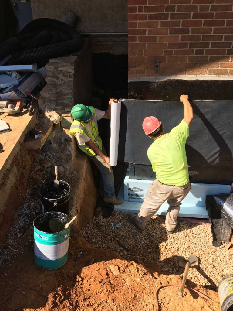Contractors install waterproof membrane to exterior commercial foundation