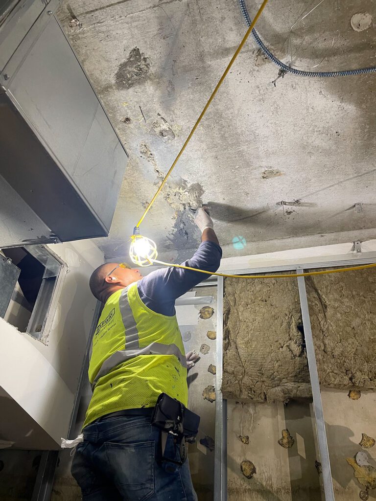 Contractor examines water damage on concrete ceiling.